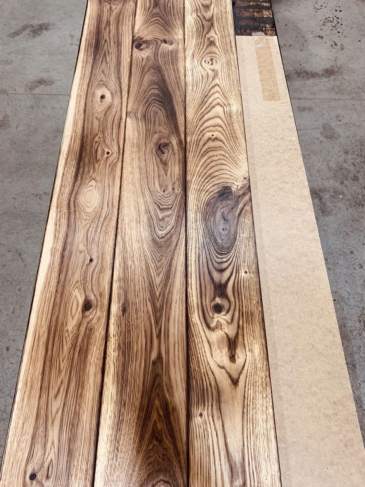 Three weathered wooden planks with dark grain patterns beside a pale board on a concrete floor