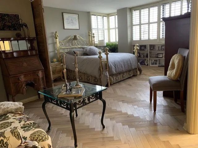 Bright bedroom with brass bed, glass coffee table, armchair, and shutters letting in daylight