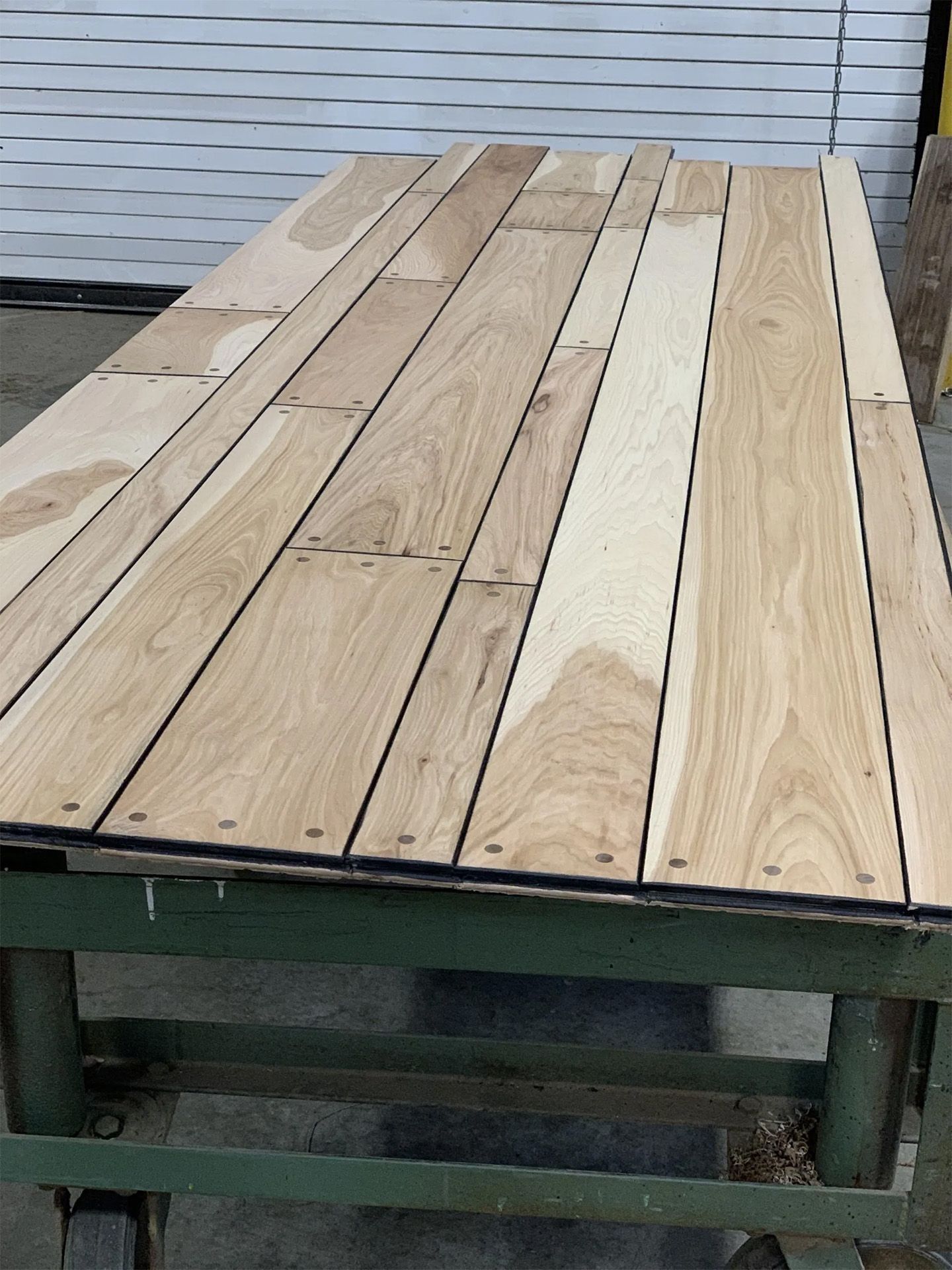 Wooden tabletop with mixed light and weathered planks on a green metal frame outdoors.