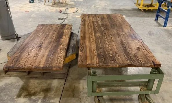 Two rustic wooden tabletop slabs on green metal stands in a workshop