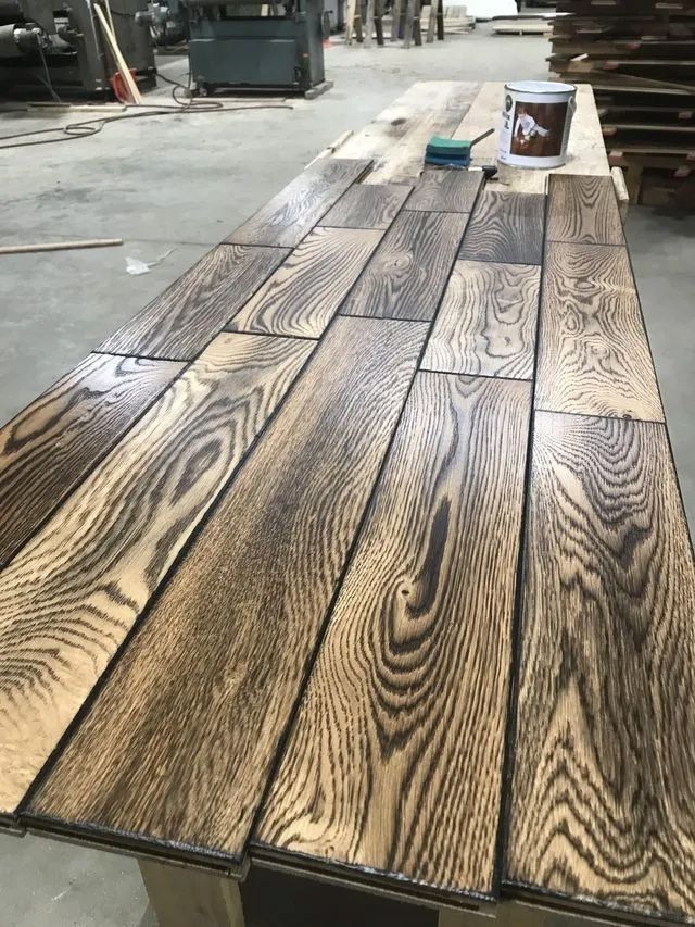 Stained wooden planks laid across a workbench with a small paint can and brush in the background