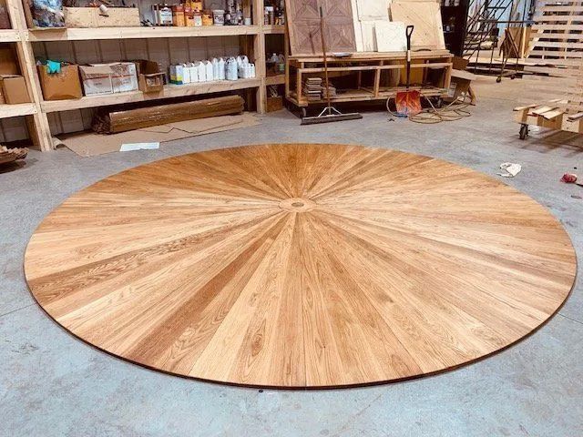 Large round wooden tabletop with a sunburst grain pattern in a workshop