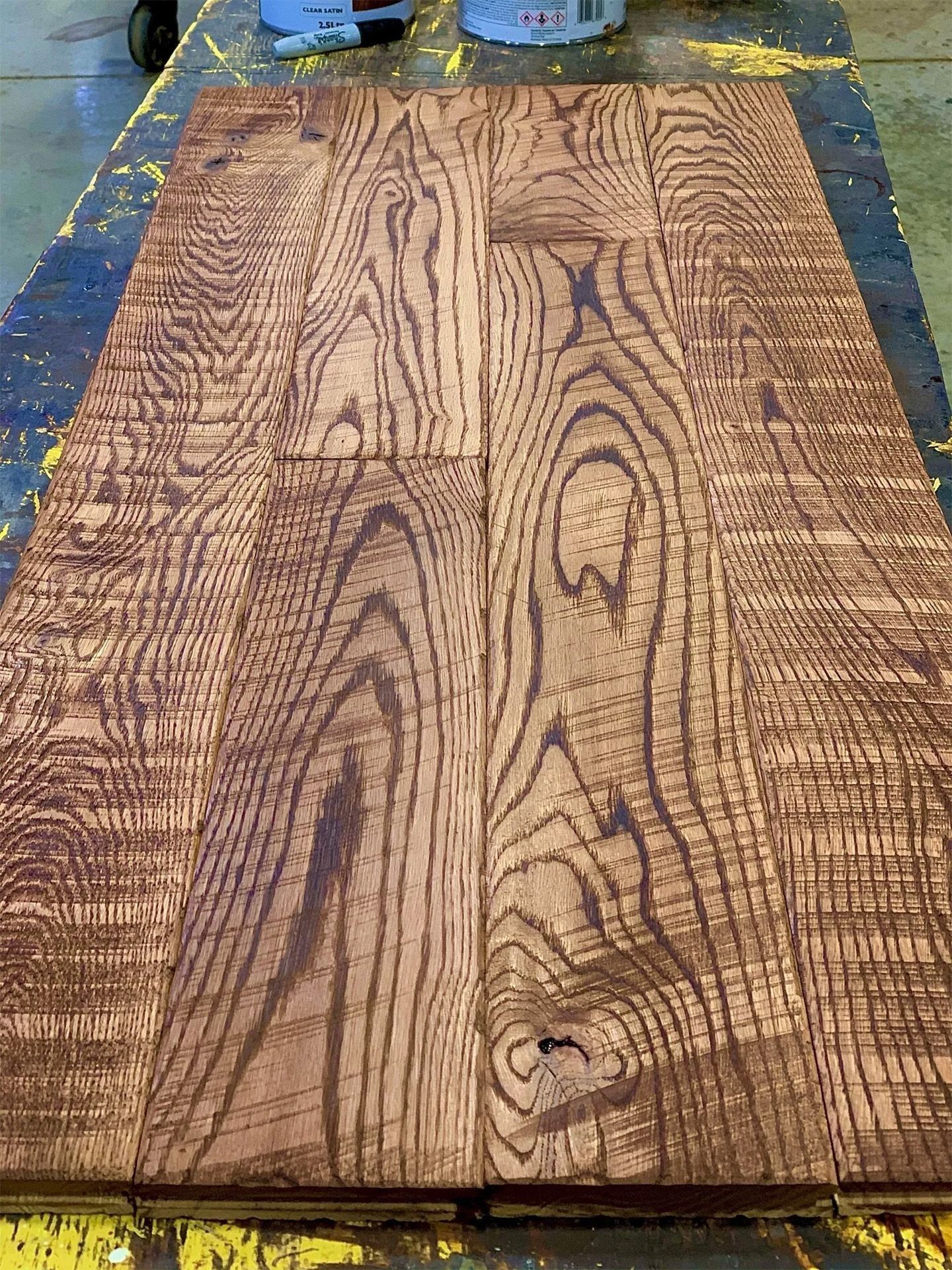 A weathered wooden board with wavy grain and a central knot on a workbench, surrounded by tools.
