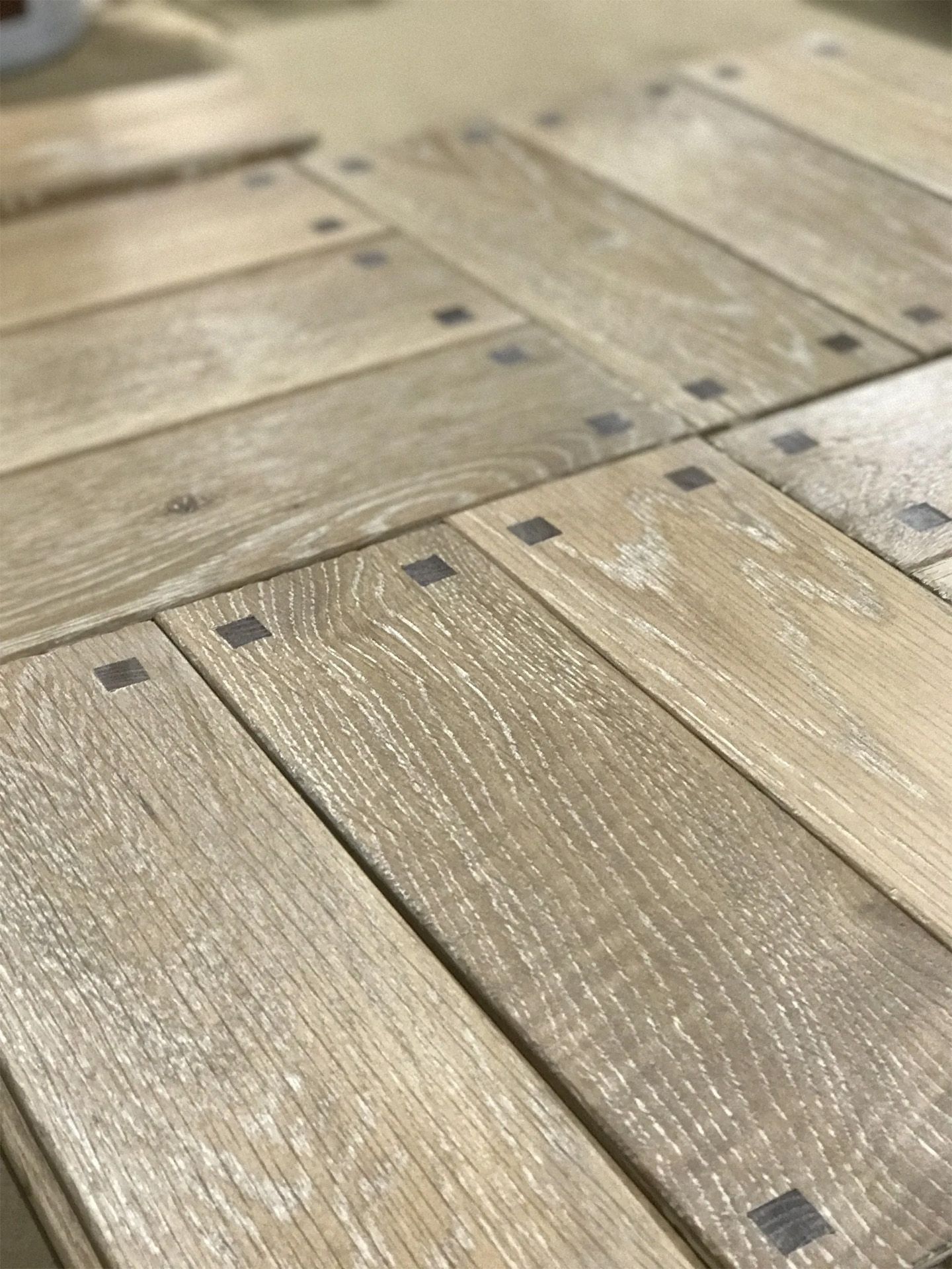 Close-up of weathered light wood planks with dark metal rivets arranged in a grid.
