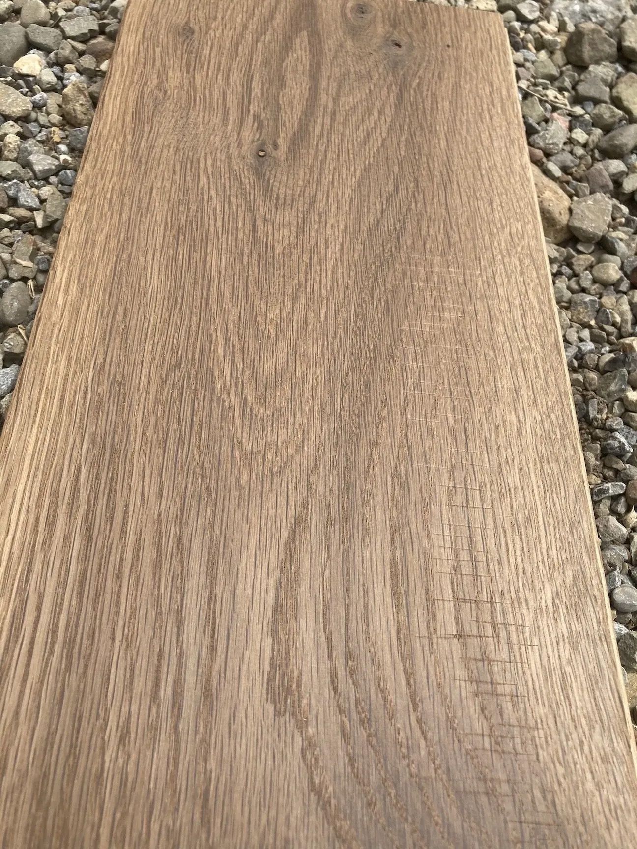 A tan wooden plank with a natural grain pattern on a gravel background