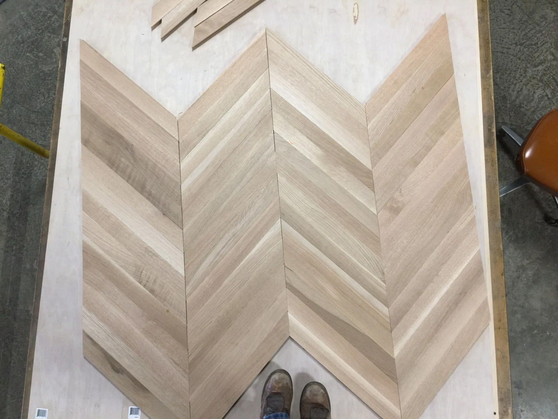 Chevron wood plank flooring laid on a floor, shown with shoes at the bottom edge.