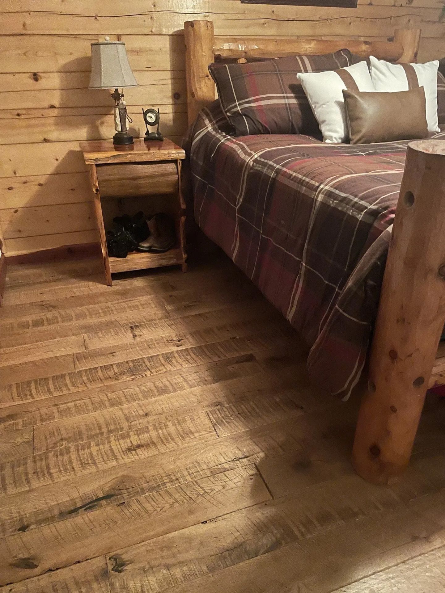 Rustic log cabin bedroom with plaid bedspread, wooden nightstand, and plank walls and floor
