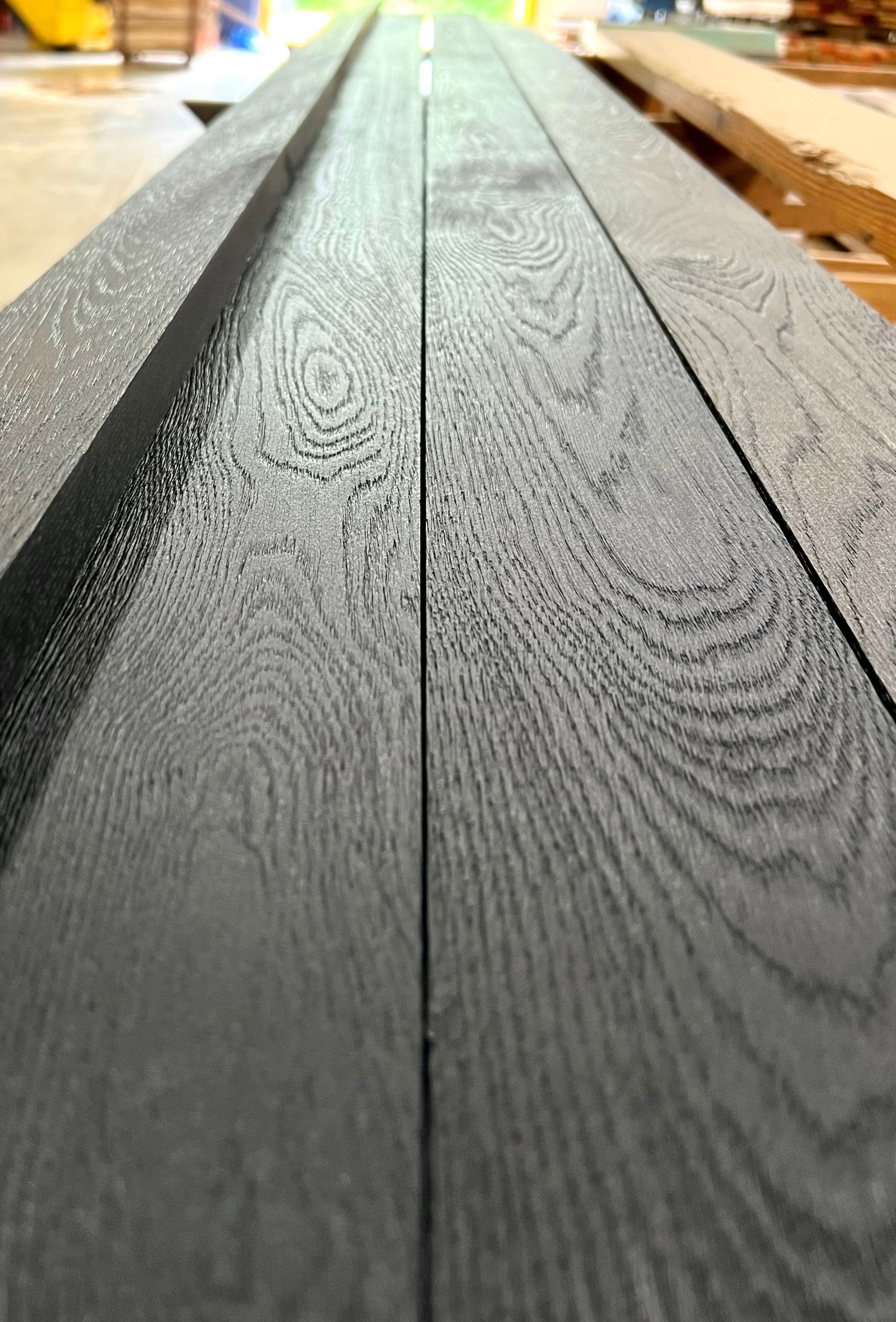 Close-up of dark gray wooden planks with visible grain, running lengthwise in a workshop setting