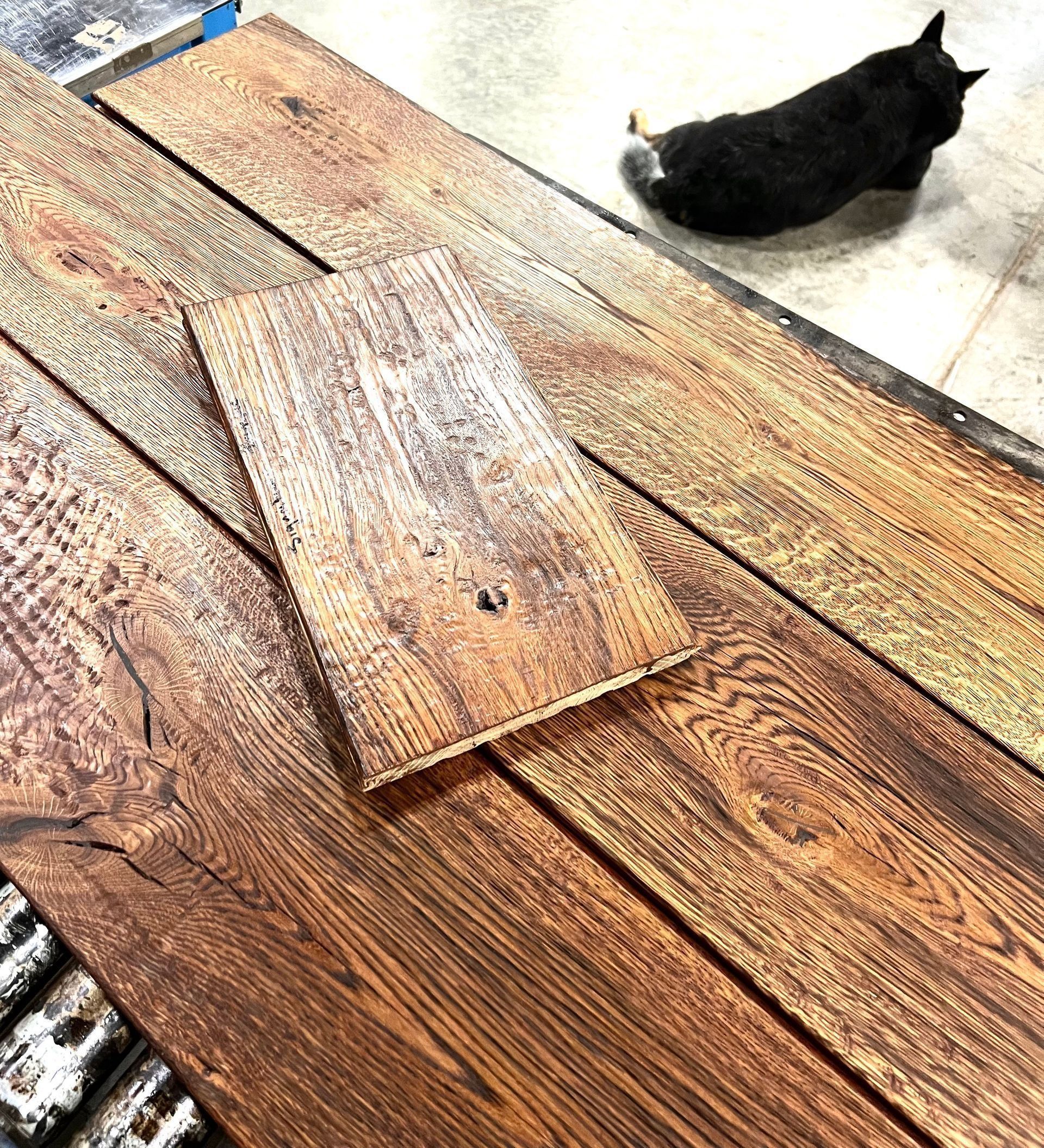 Black cat lying on a tiled floor beside stacked weathered wooden boards