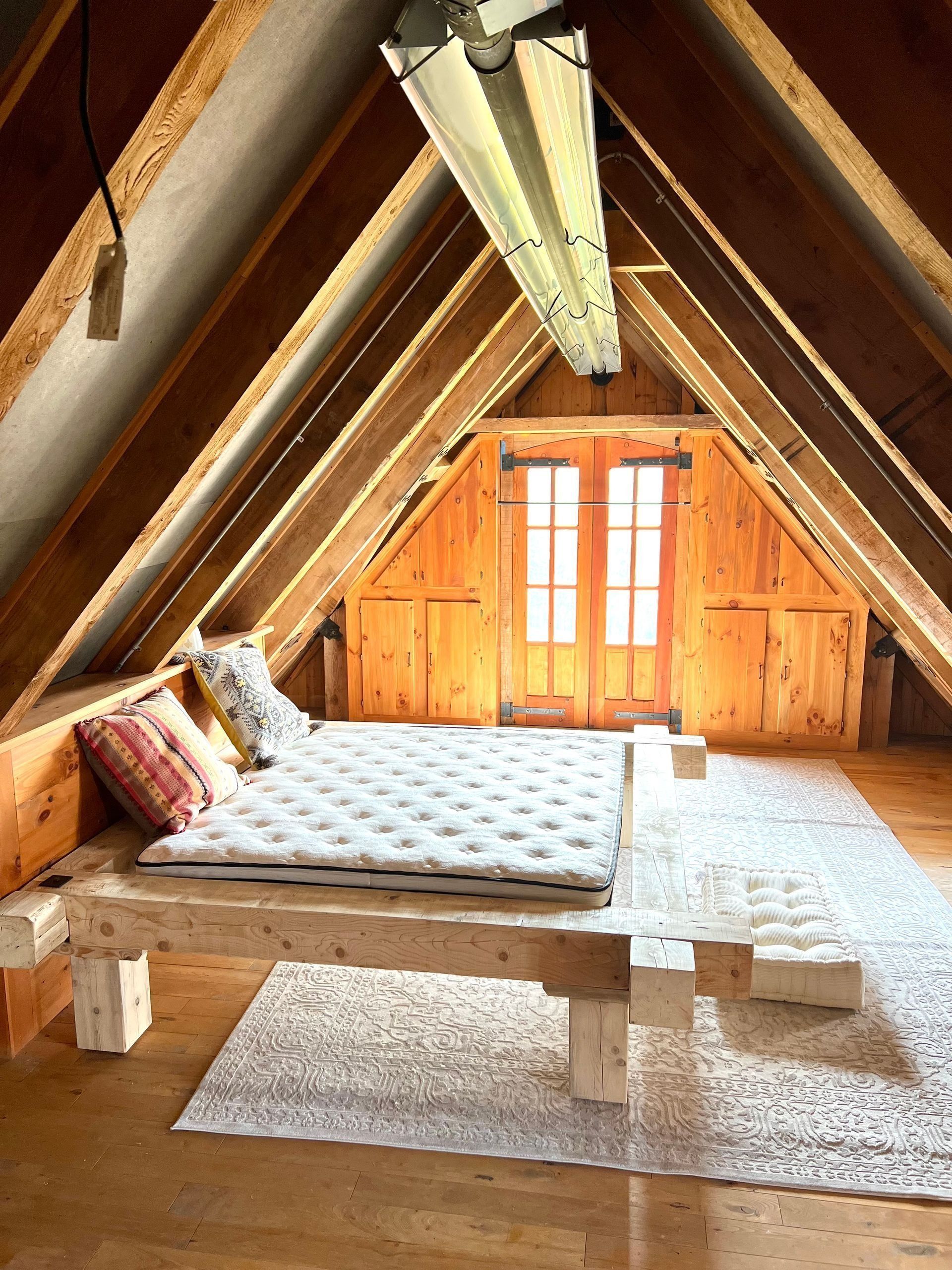 A cozy attic bedroom with a wooden bed, bright orange curtains, and slanted beams.