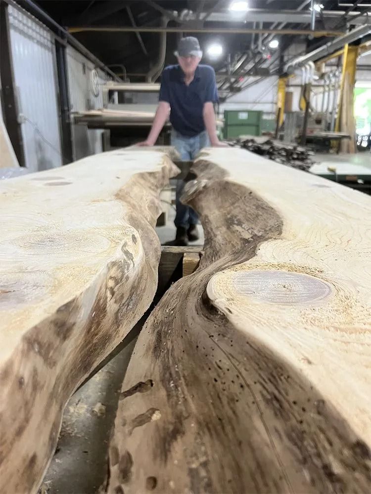 Worker standing on a large live-edge wood slab in a workshop