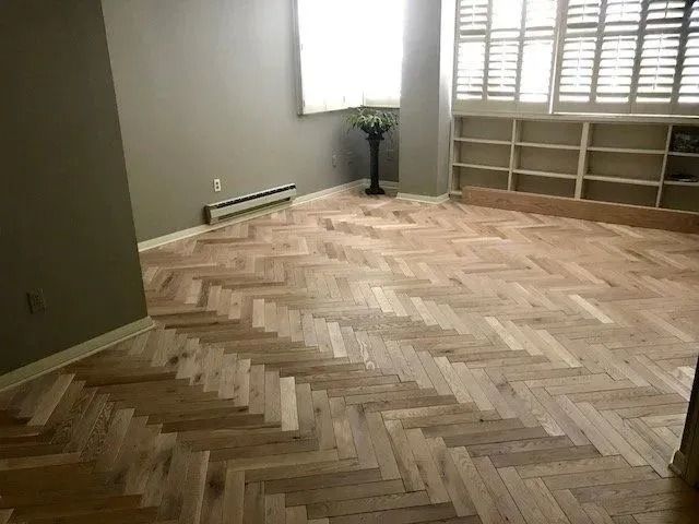 Empty room with herringbone wood floor, window, built-in shelves, and a floor lamp