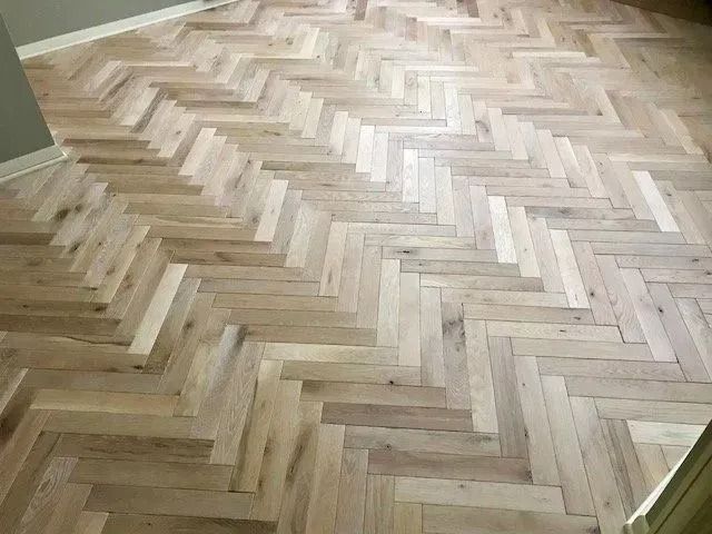 Light wood herringbone parquet flooring with a few darker patches near the edges