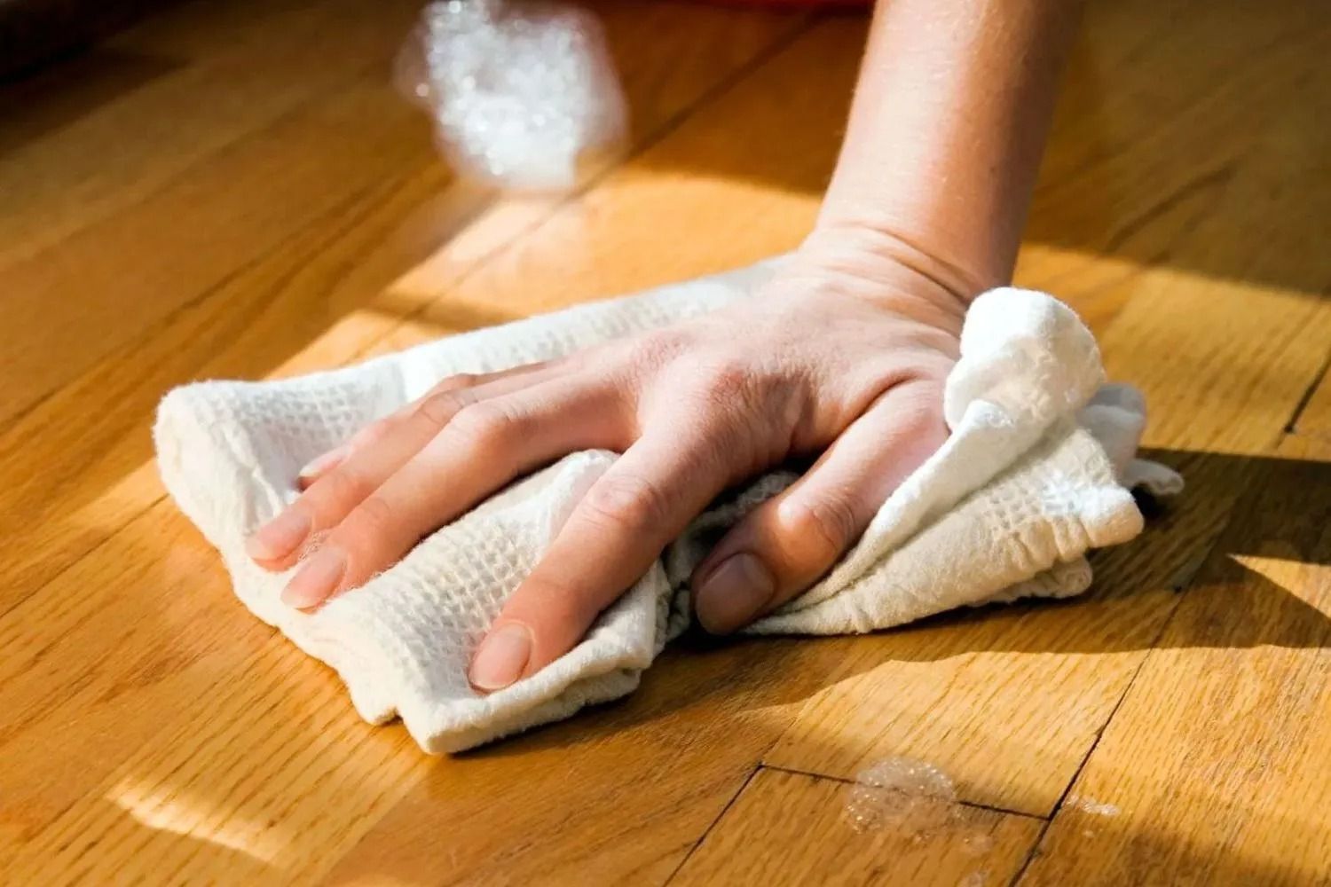 Hand wiping a wooden floor with a cloth, with steam rising in the background