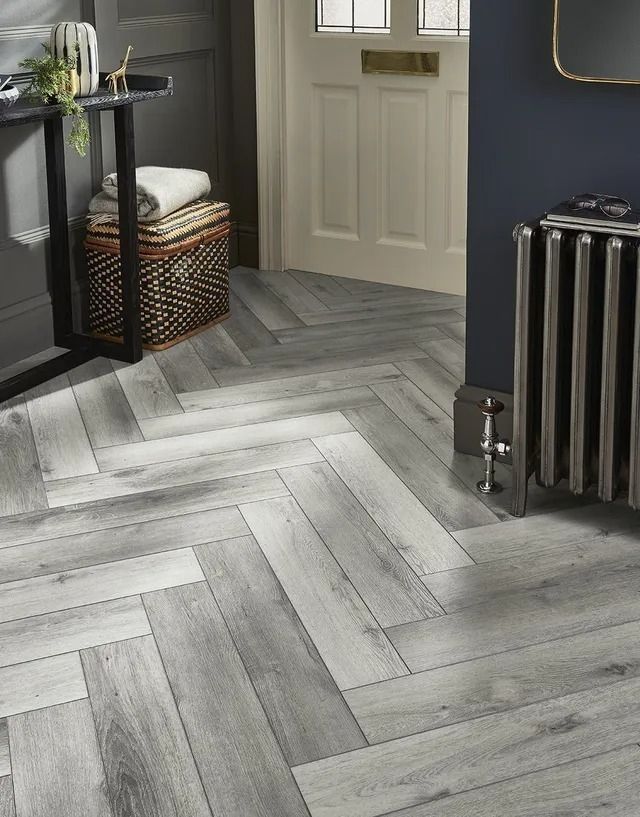 Modern hallway with gray herringbone floor, dark wall shelf, and a vintage radiator beside a door.