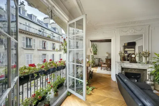 Bright Paris apartment living room with open balcony doors, flowers, fireplace, and street view