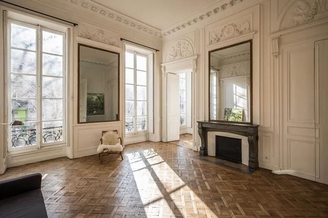 Elegant empty room with parquet floor, tall windows, ornate molding, and a fireplace.