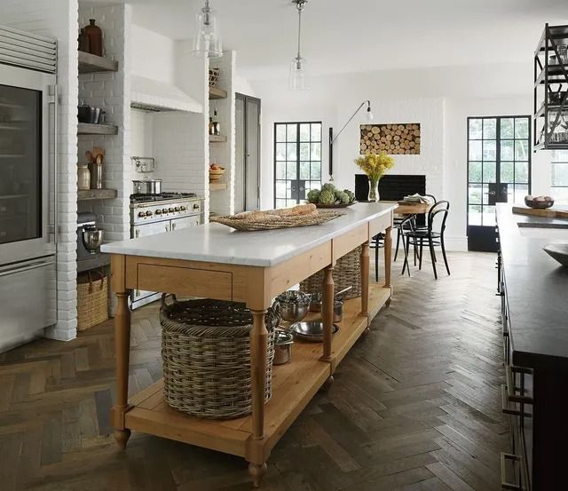 Bright modern kitchen with a large wooden island, woven baskets, and dining table by windows