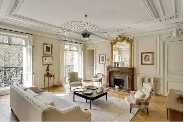 Elegant white living room with fireplace, chandelier, large windows, and classic furniture