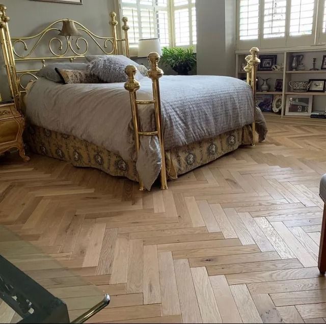 Elegant gold-canopy bed in a bright bedroom with herringbone wood floor and large windows
