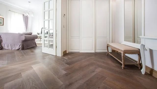 Bright bedroom with white walls, herringbone wood floor, bed, open glass doors, and a wooden bench