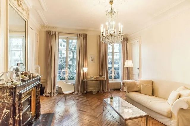 Elegant living room with chandelier, cream sofa, fireplace, and tall windows with curtains