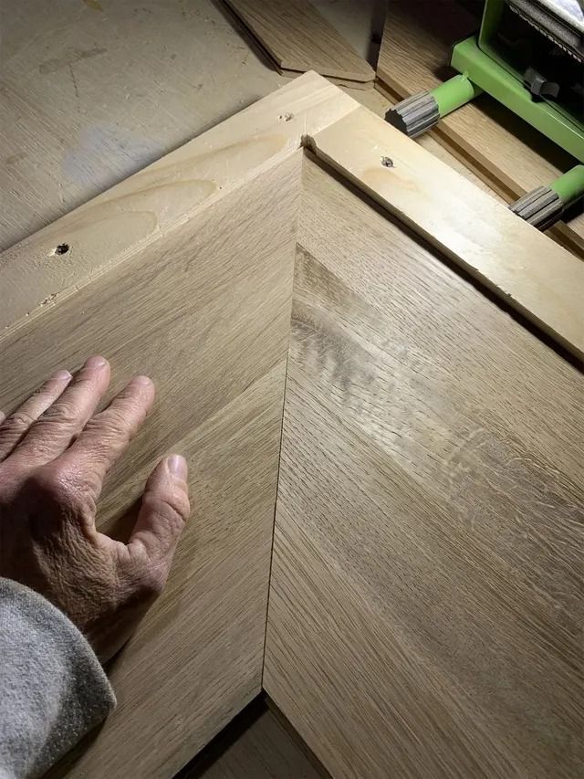 Hand guiding a wooden board into a mitered corner joint on a workbench