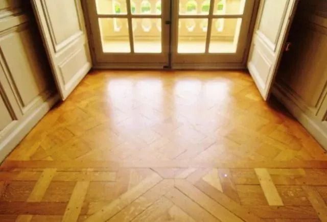 Empty sunlit room with polished herringbone wood floor and French doors opening outside