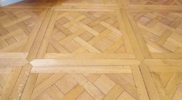 Close-up of a patterned wooden parquet floor with a light-colored strip across the center.