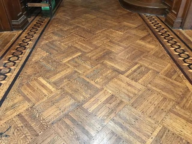 Patterned wooden parquet floor in a room, with a herringbone center and dark border trim.