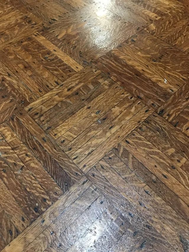 Close-up of worn brown wooden parquet flooring with a glossy reflection.