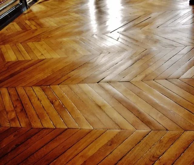 Wooden herringbone parquet floor with warm brown tones and glossy light reflections