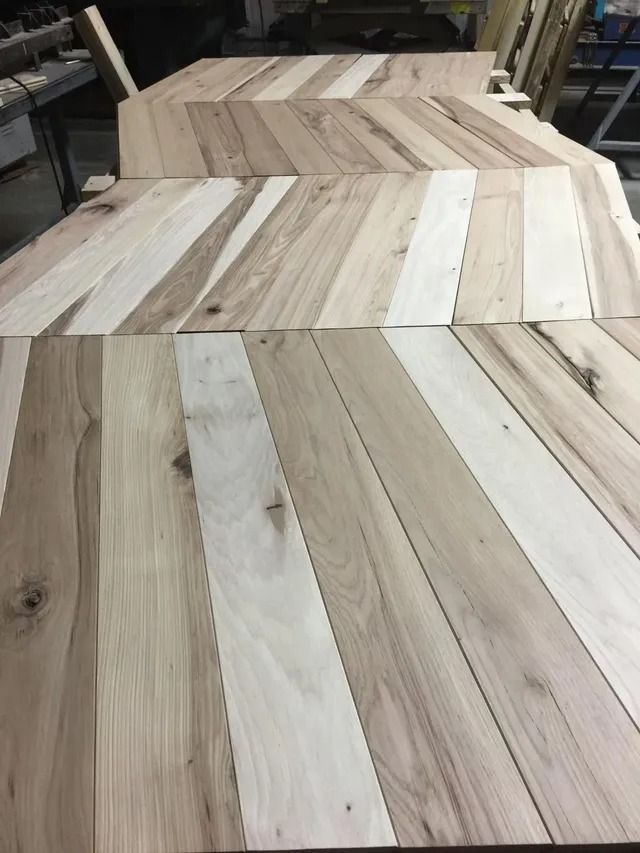Stacked wooden tabletops with light and dark chevron-pattern wood planks in a workshop
