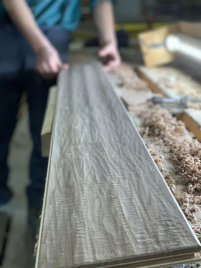 Hands planing a long wooden board on a workbench in a workshop