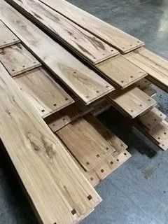 Stacked weathered wooden planks with drilled holes, piled on a concrete floor.