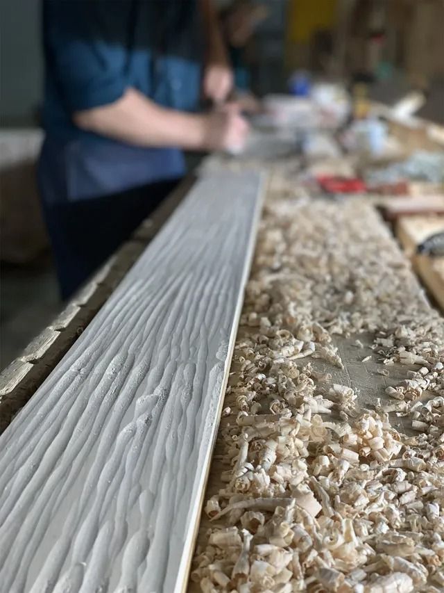 Close-up of a person smoothing white mortar along a textured surface in a workshop