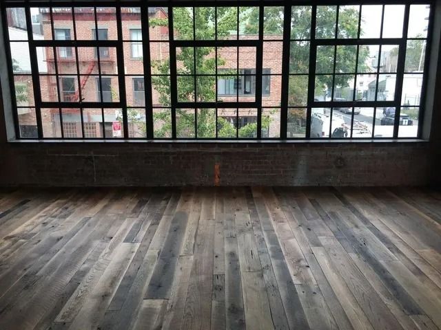 Empty loft-style room with large grid windows and weathered wooden floorboards.