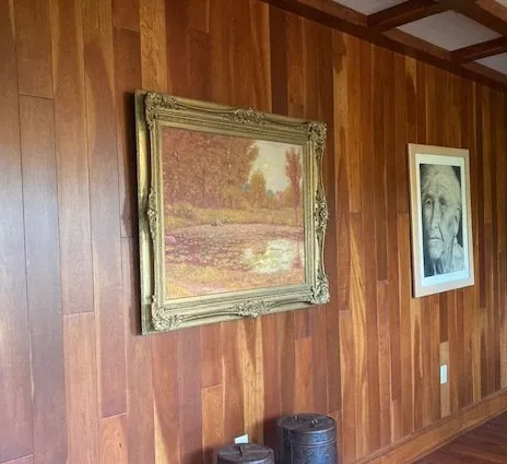 Wood-paneled wall with two framed paintings and small objects on a ledge