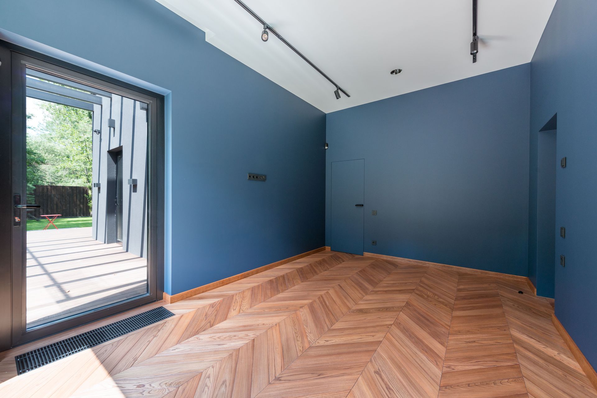 Blue-walled empty room with herringbone wood floor and open glass door to a patio