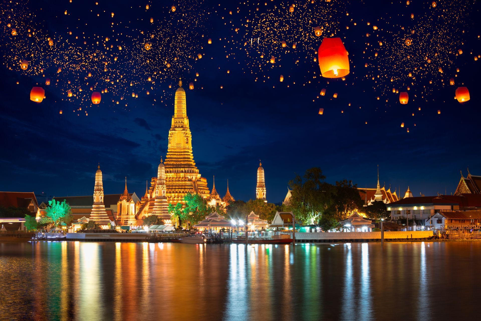 Night view of a golden temple by a river, with lanterns glowing overhead and reflections on the water