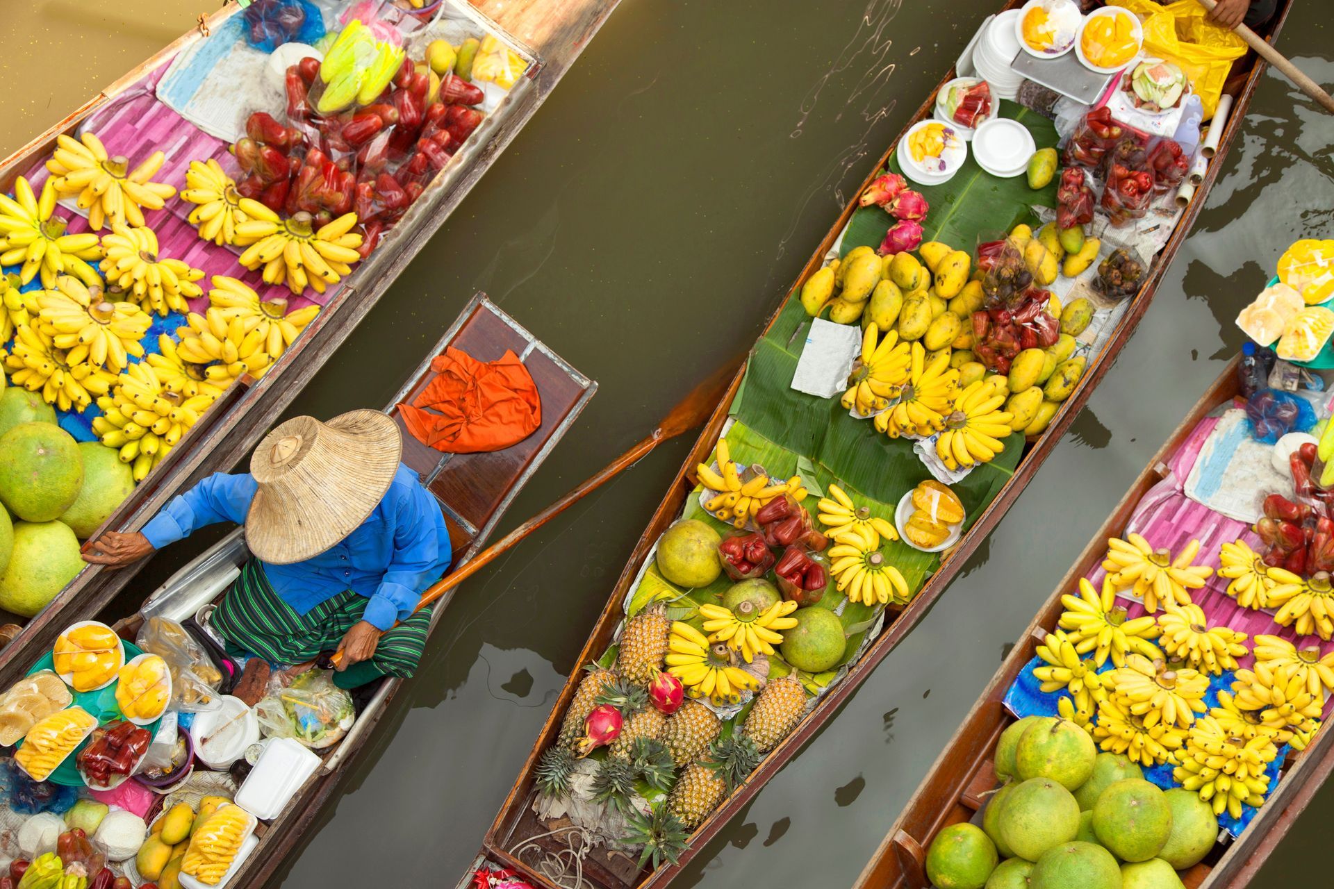 Flower-filled boats on a canal, with a person in a blue shirt paddling between colorful floral arrangements