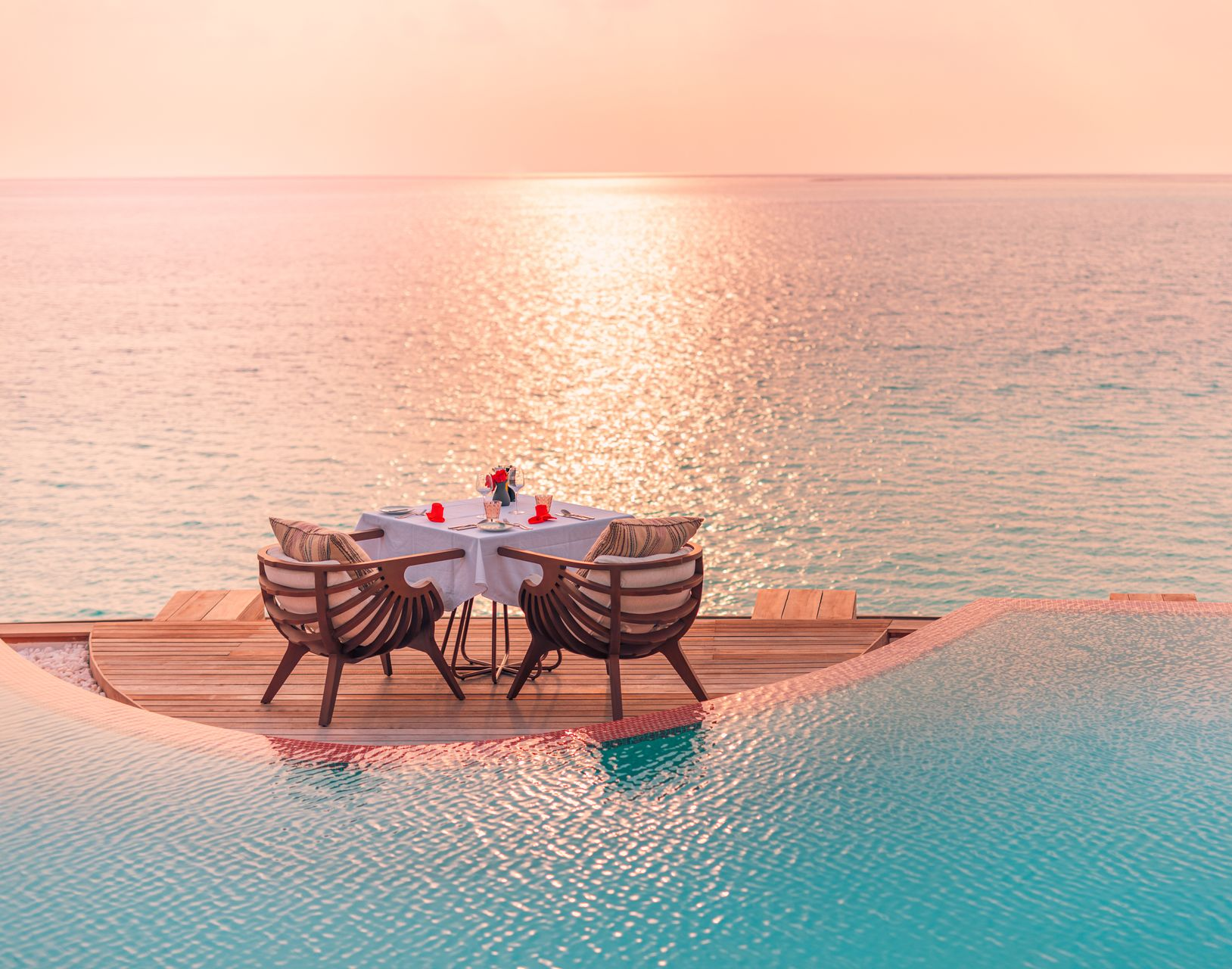 Sunset dining table on a poolside deck overlooking calm ocean water