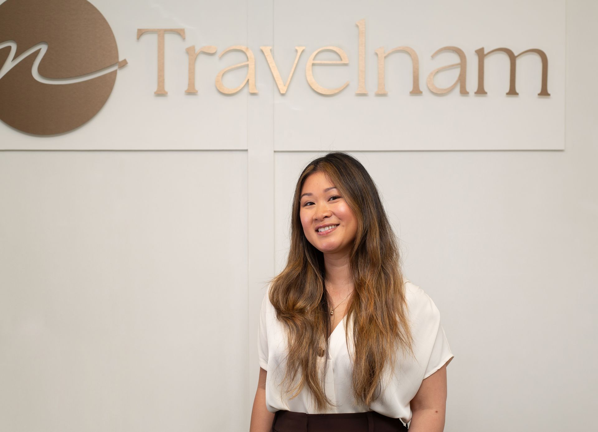 Woman smiling beside the Travelnam sign in a bright office lobby