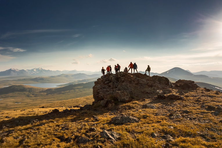 Hikers standing on a rocky hilltop overlooking a vast valley at sunset