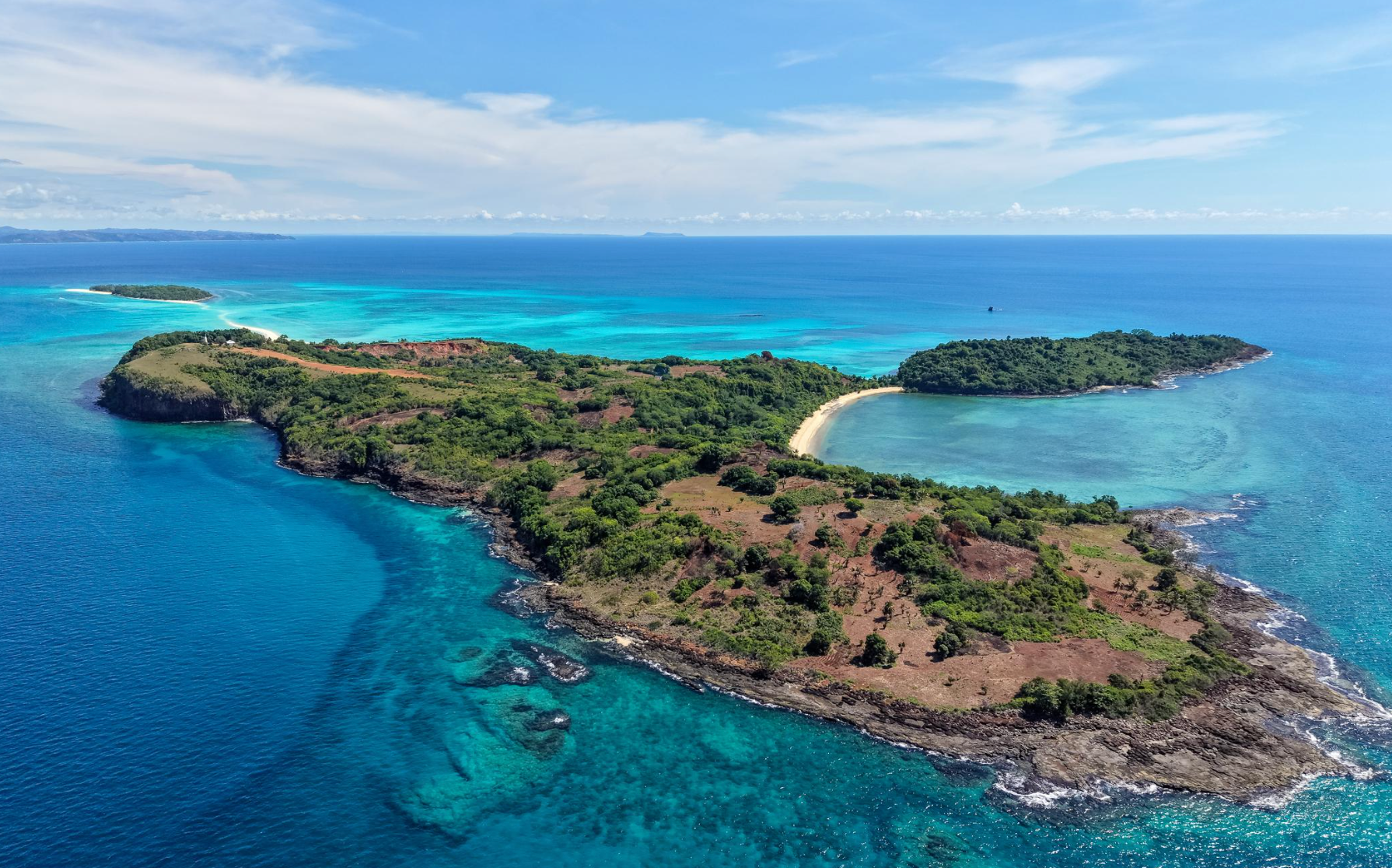 Aerial view of a small green island surrounded by bright blue ocean and sandy shoreline