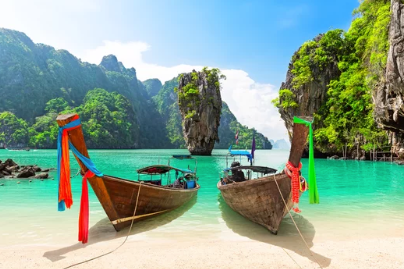 Two long-tail boats on a turquoise beach with limestone cliffs and a clear blue sky