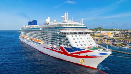 Large white cruise ship with red accents sailing near a tropical harbor