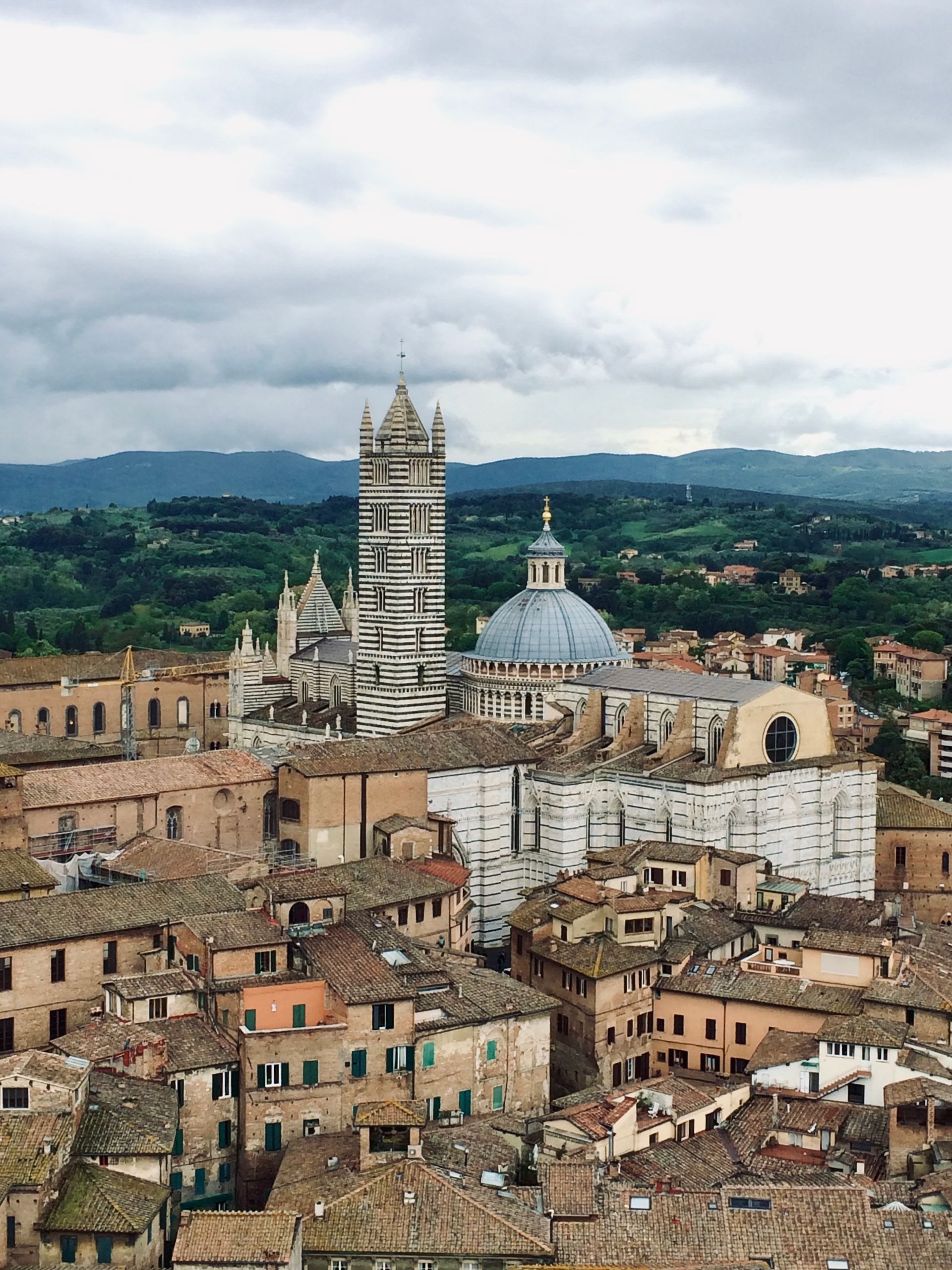 Panoramic view of Siena, Italy, with striped cathedral tower and domed church above terracotta rooftops