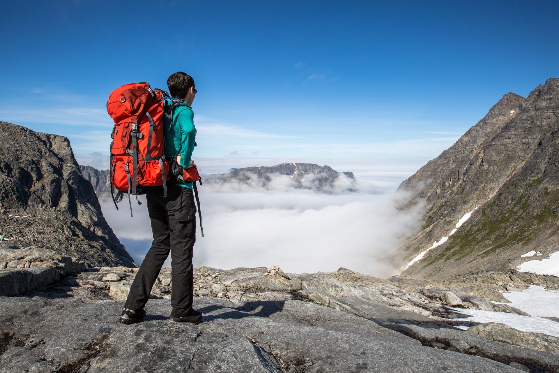 Hiker with red backpack standing on a rocky mountain ridge above a sea of clouds