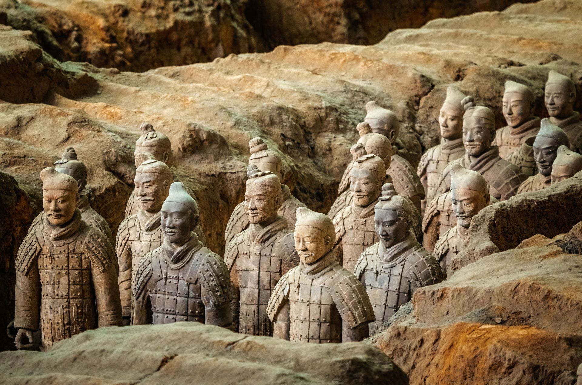 Terracotta warrior statues arranged in rows among rocky earth tones